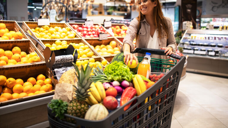 Beautiful,Smiling,Woman,Pushing,Shopping,Cart,And,Taking,Fruits,Off